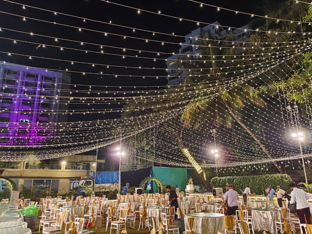 Open-air wedding lawn setup at night with fairy lit canopy and guest dining